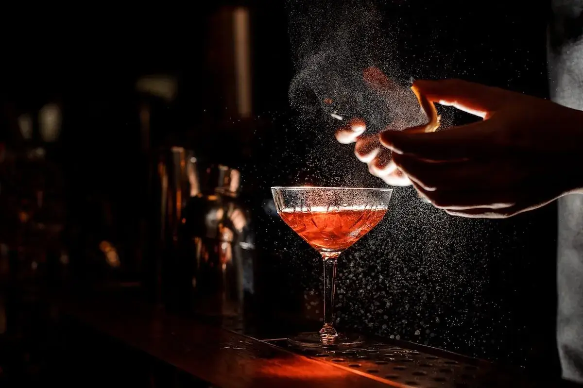 A bartender spraying an orange peel over a cocktail