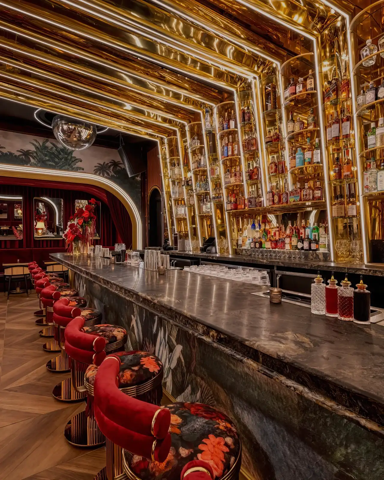 The bar at Tell Your Friends with gold shelving and red velvet stools